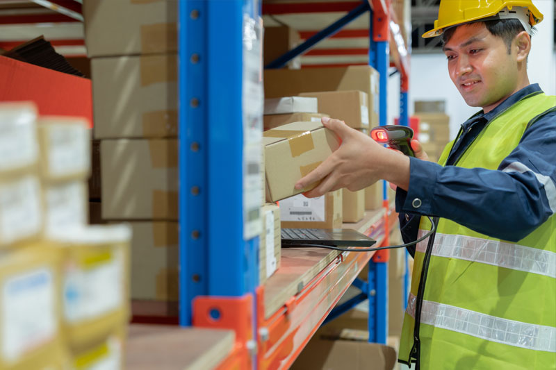 Warehouse worker scanning and handling parcels on warehouse shelving
